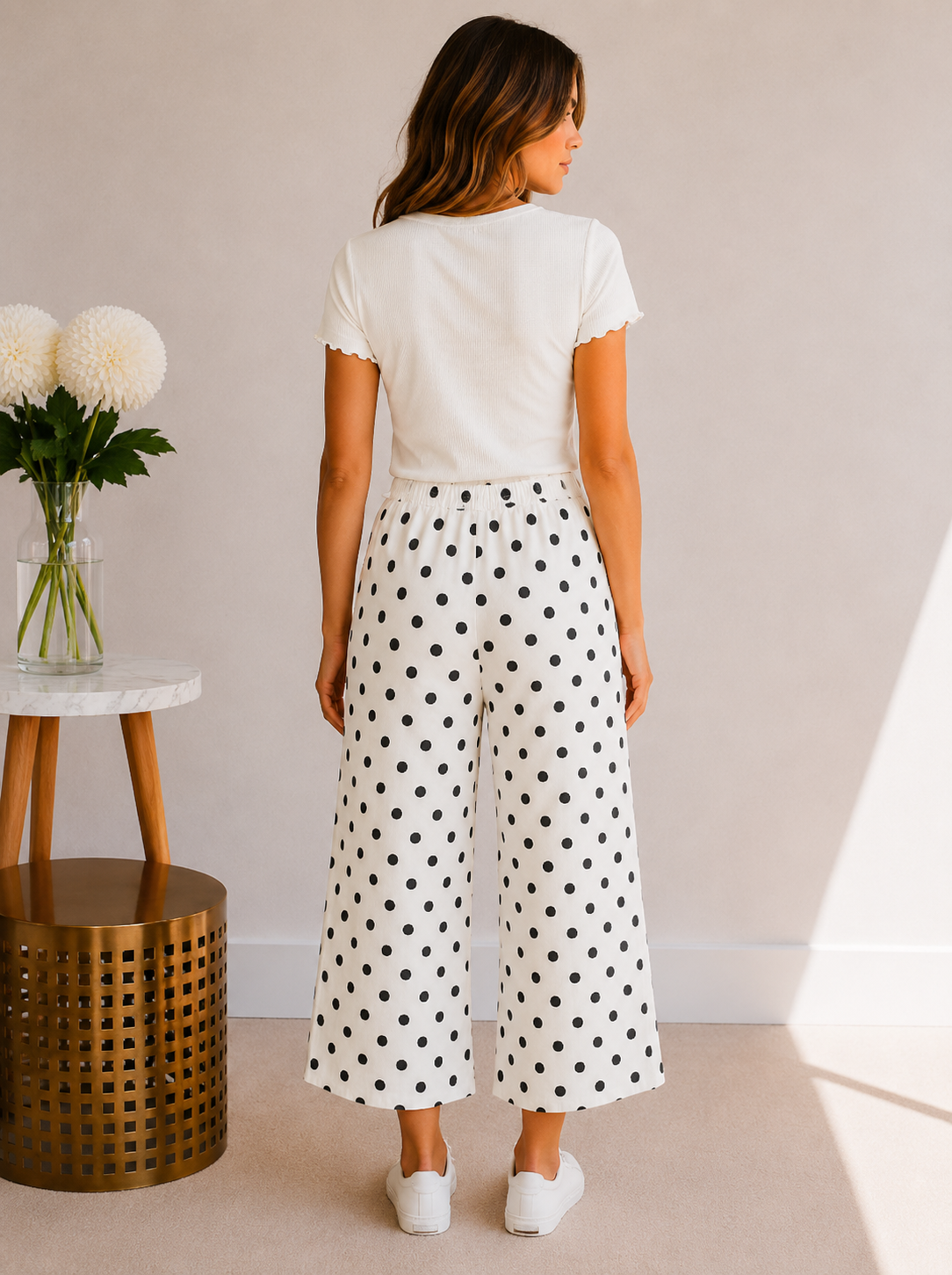 Woman wearing a white t-shirt and polka dot pants in a minimalistic room.