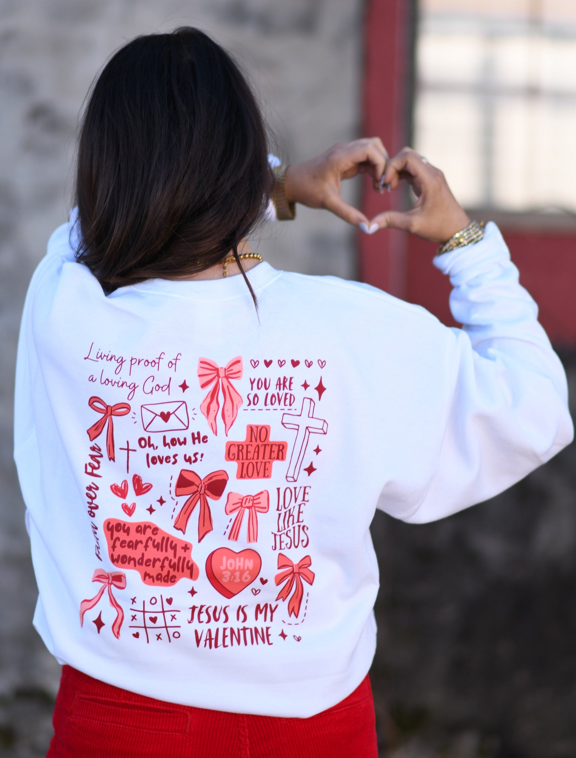 Person wearing a white sweatshirt with red graphics and text, standing against a blurred background.