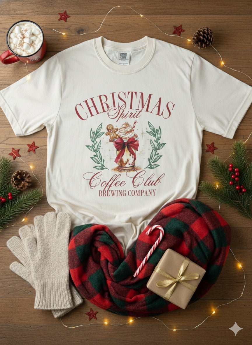 White t-shirt with Christmas design, mug with hot chocolate, plaid blanket, candy canes, and gift on a wooden surface.