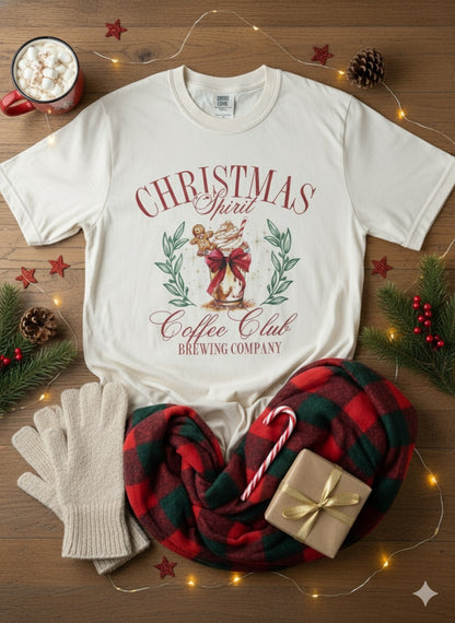White t-shirt with Christmas design, mug with hot chocolate, plaid blanket, candy canes, and gift on a wooden surface.