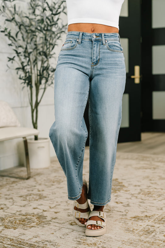 Person wearing light blue jeans and white sandals in an outdoor setting.