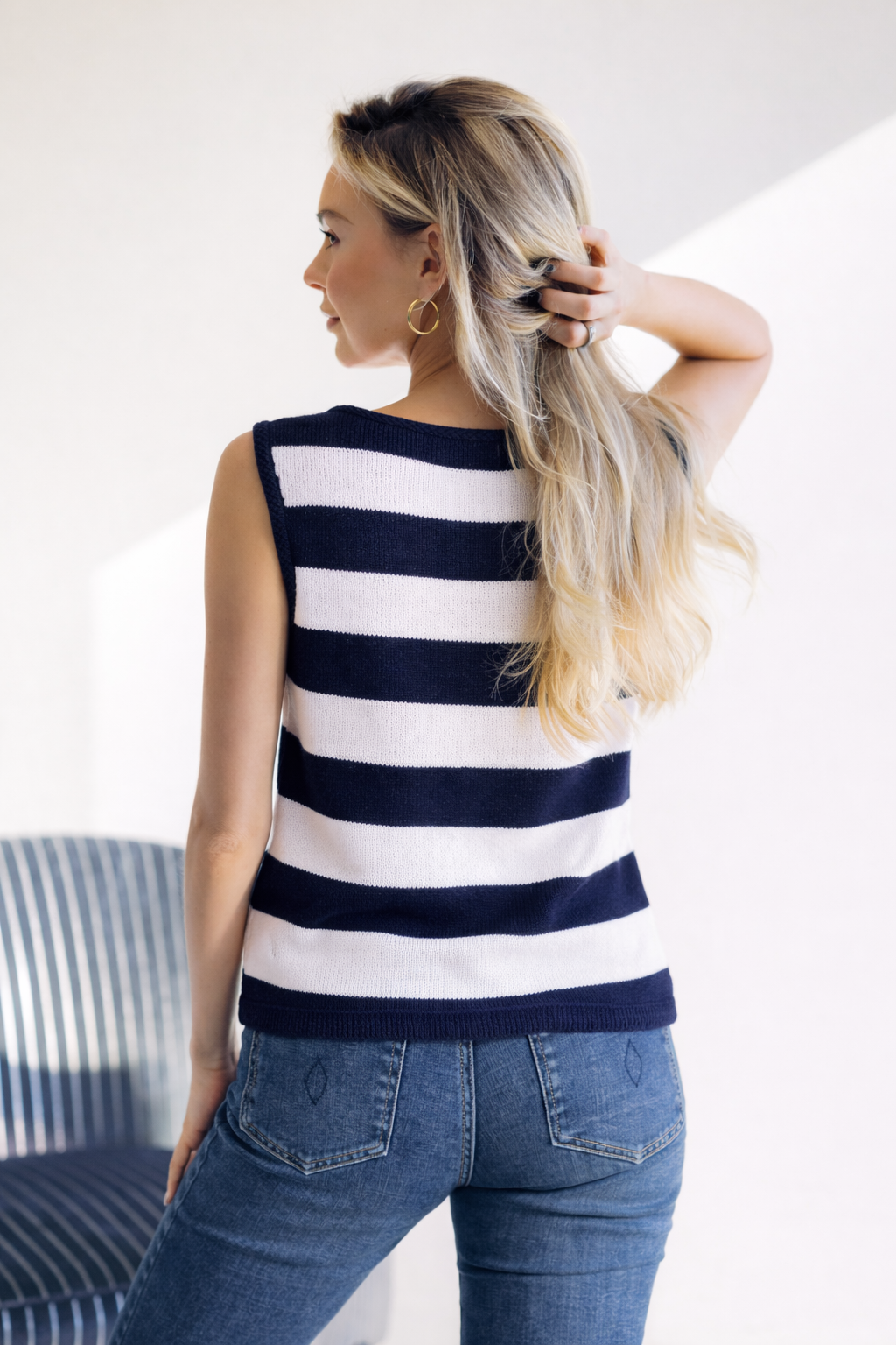Woman wearing a navy and white striped sleeveless top and blue jeans, standing indoors.