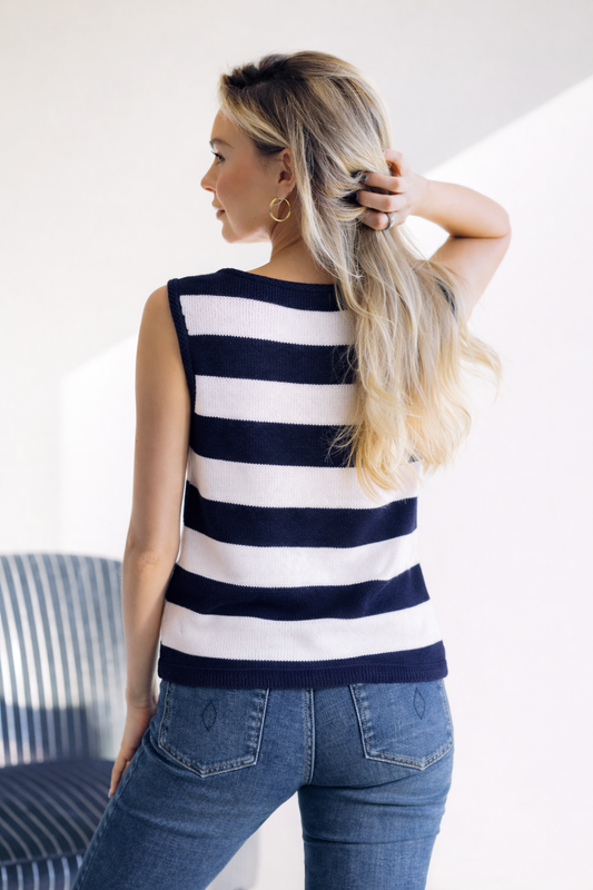 Woman wearing a navy and white striped sleeveless top and blue jeans, standing indoors.