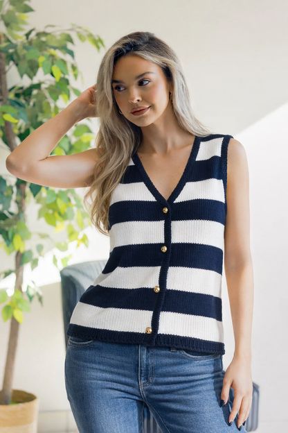 Woman wearing a navy and white striped sleeveless cardigan with a blurred indoor background