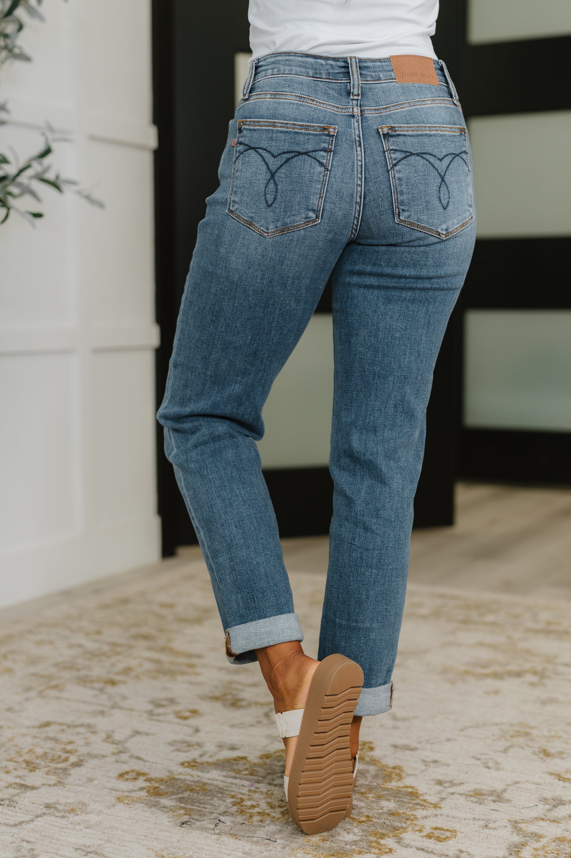 Person wearing blue jeans with heart designs on the back pockets, standing indoors.