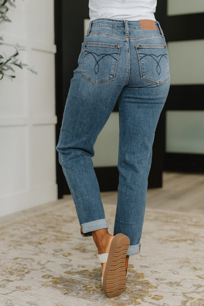 Person wearing blue jeans with heart designs on the back pockets, standing indoors.