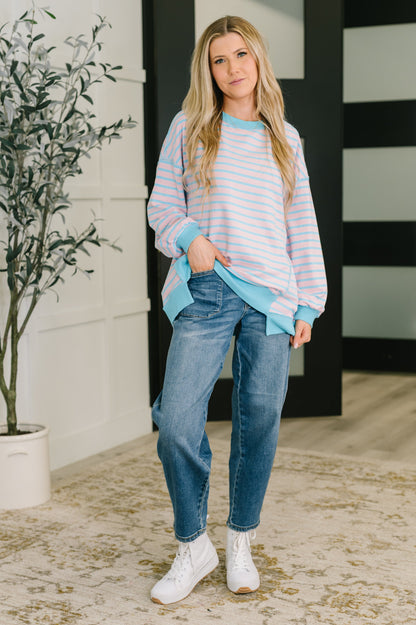 Woman wearing a striped sweater and jeans standing indoors with a plant in the background