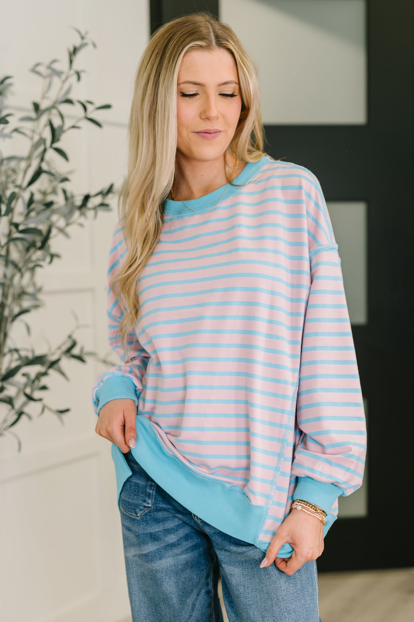Woman wearing a striped sweater and jeans indoors with a plant in the background