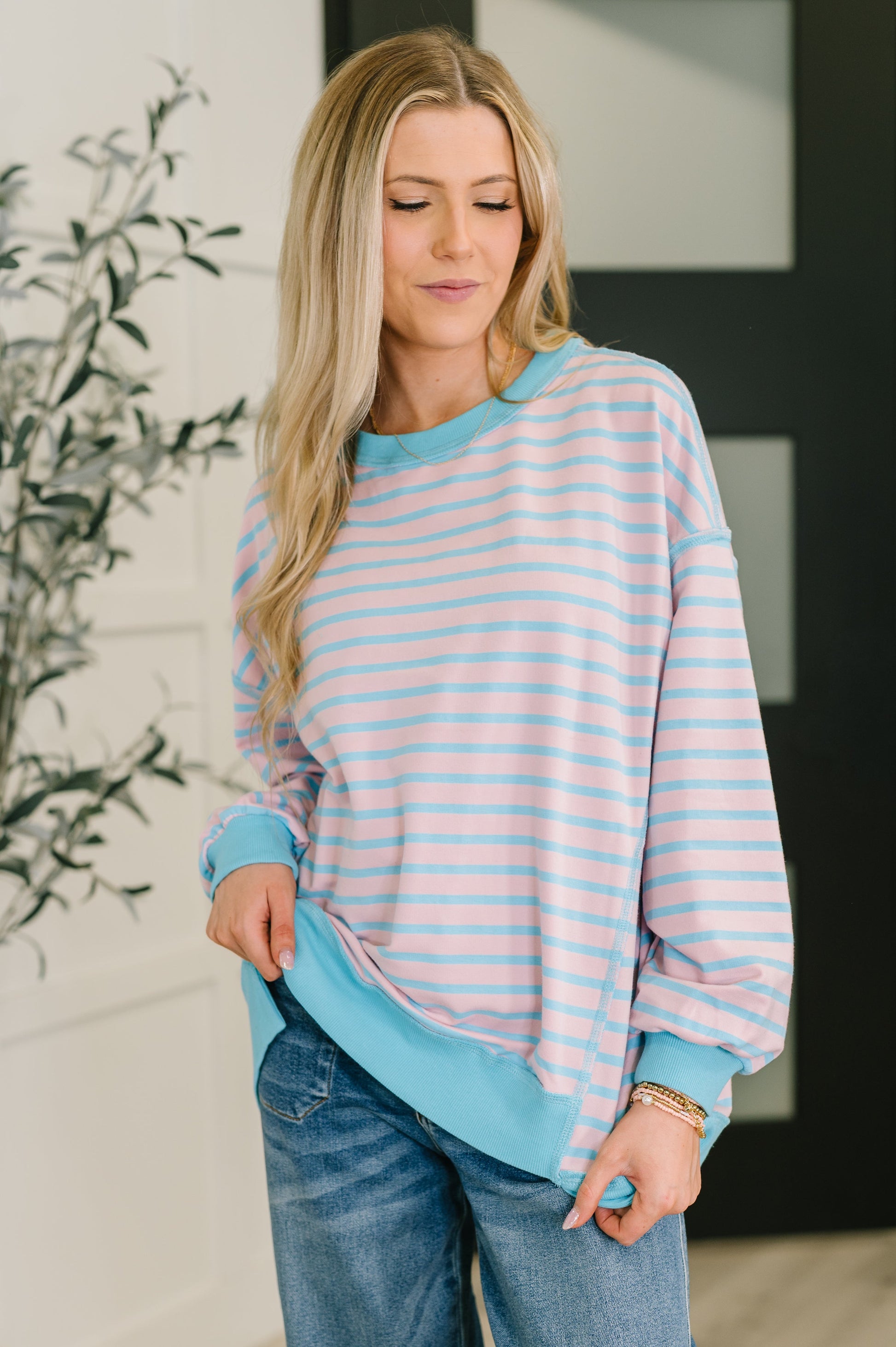 Woman wearing a striped sweater and jeans indoors with a plant in the background