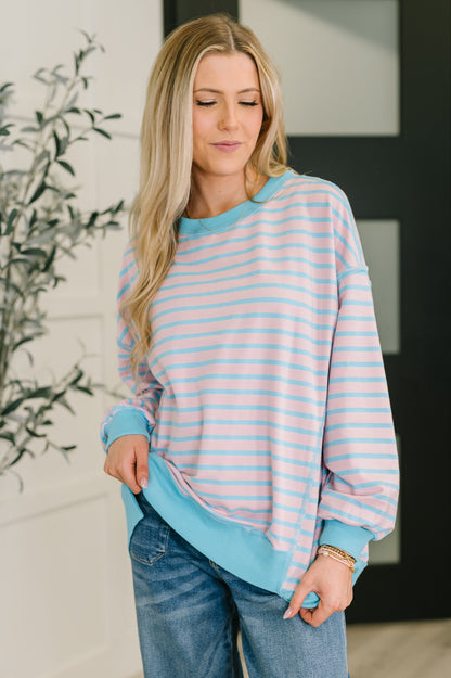 Woman wearing a striped sweater and jeans indoors with a plant in the background