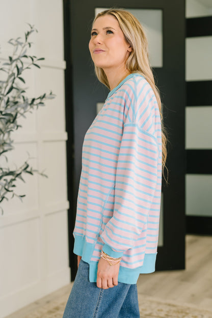 Woman wearing a light blue and pink striped sweater and jeans indoors.