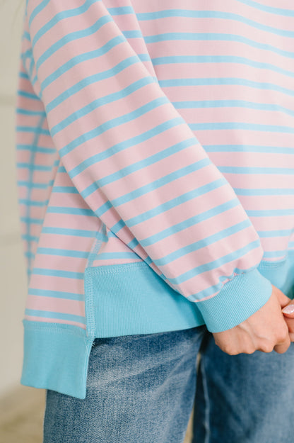 Close-up of a person wearing a pink and blue striped sweater with denim pants.