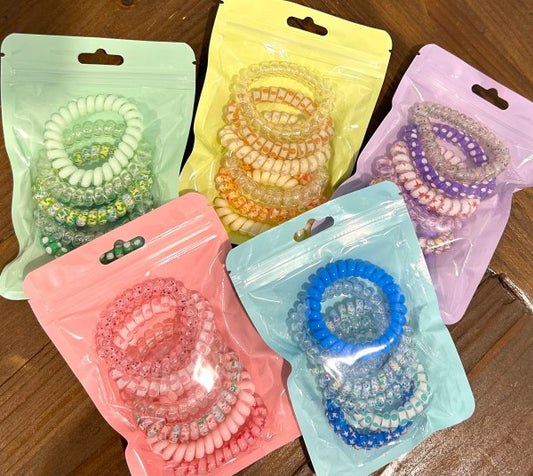 Five packages of colorful hair ties on a wooden surface