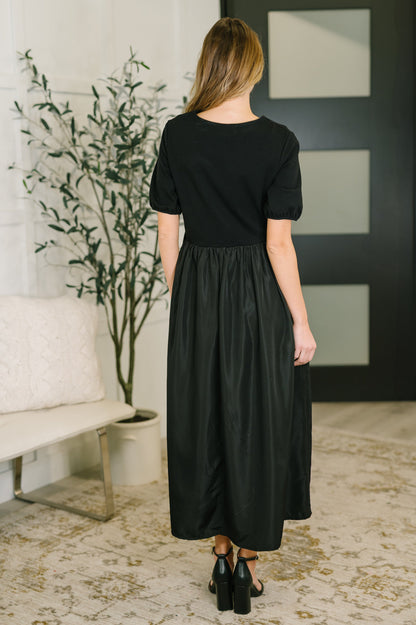Woman wearing a black dress standing in a room with a plant and wall art.