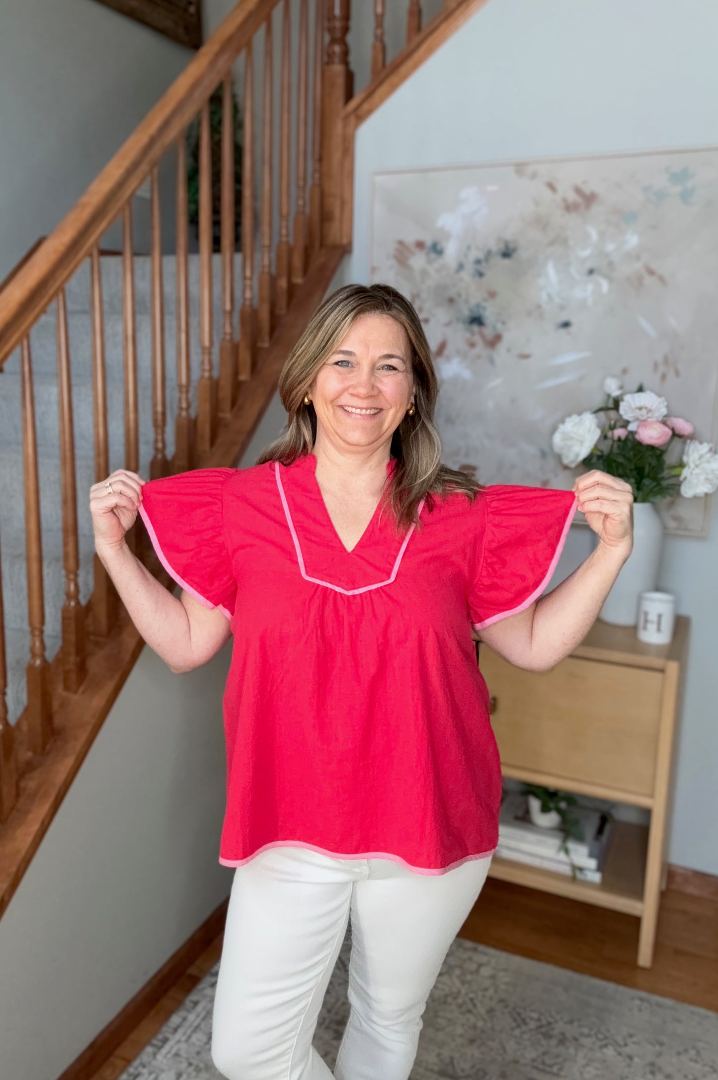 Woman wearing a red blouse with white trim in a home setting.