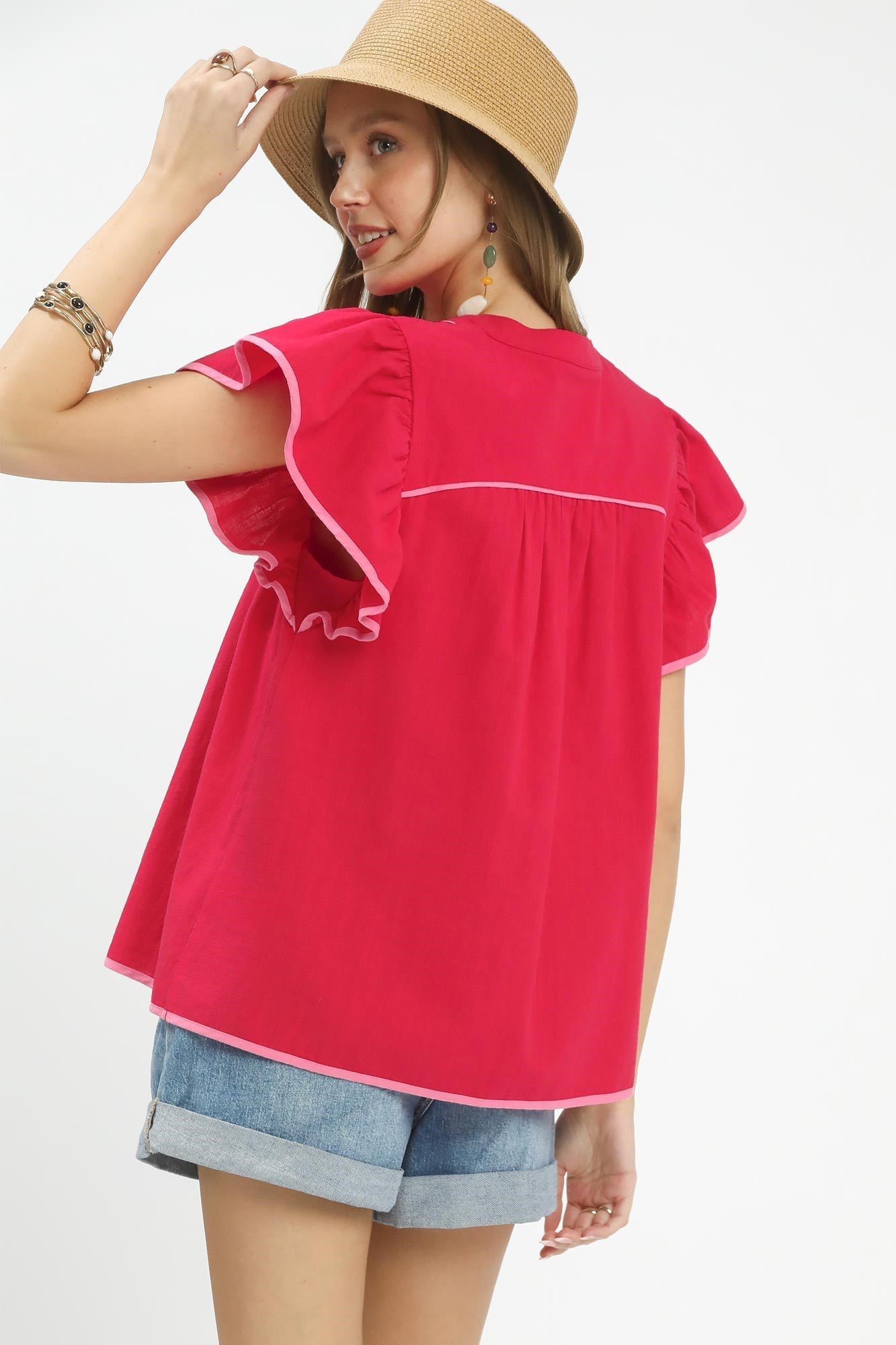 Woman wearing a bright pink top with white trim and denim shorts on a plain background