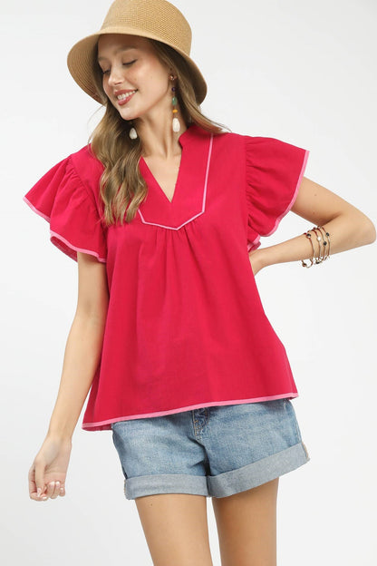 Woman wearing a red blouse with ruffled sleeves and denim shorts on a white background