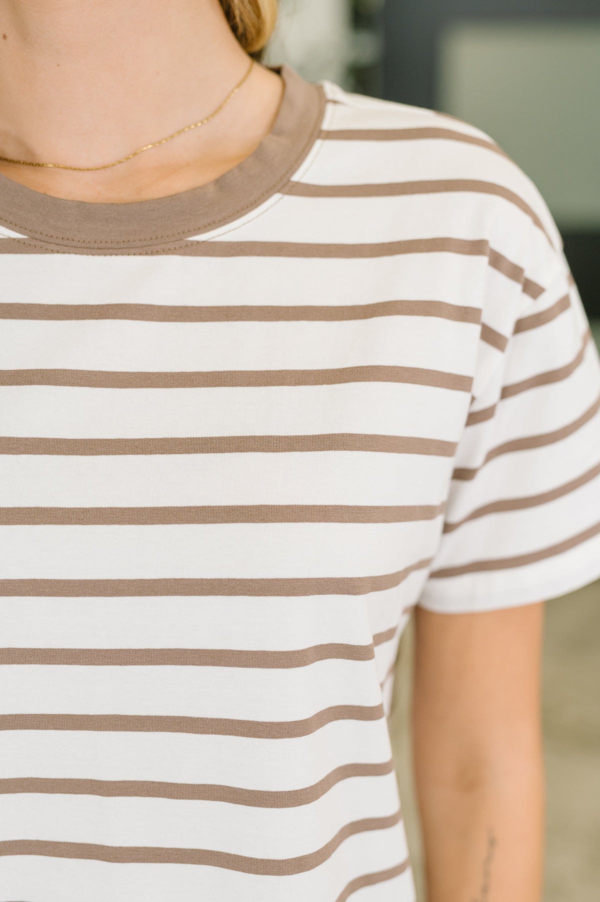 A close-up of a person wearing a short-sleeve crewneck t-shirt with horizontal brown and white stripes.