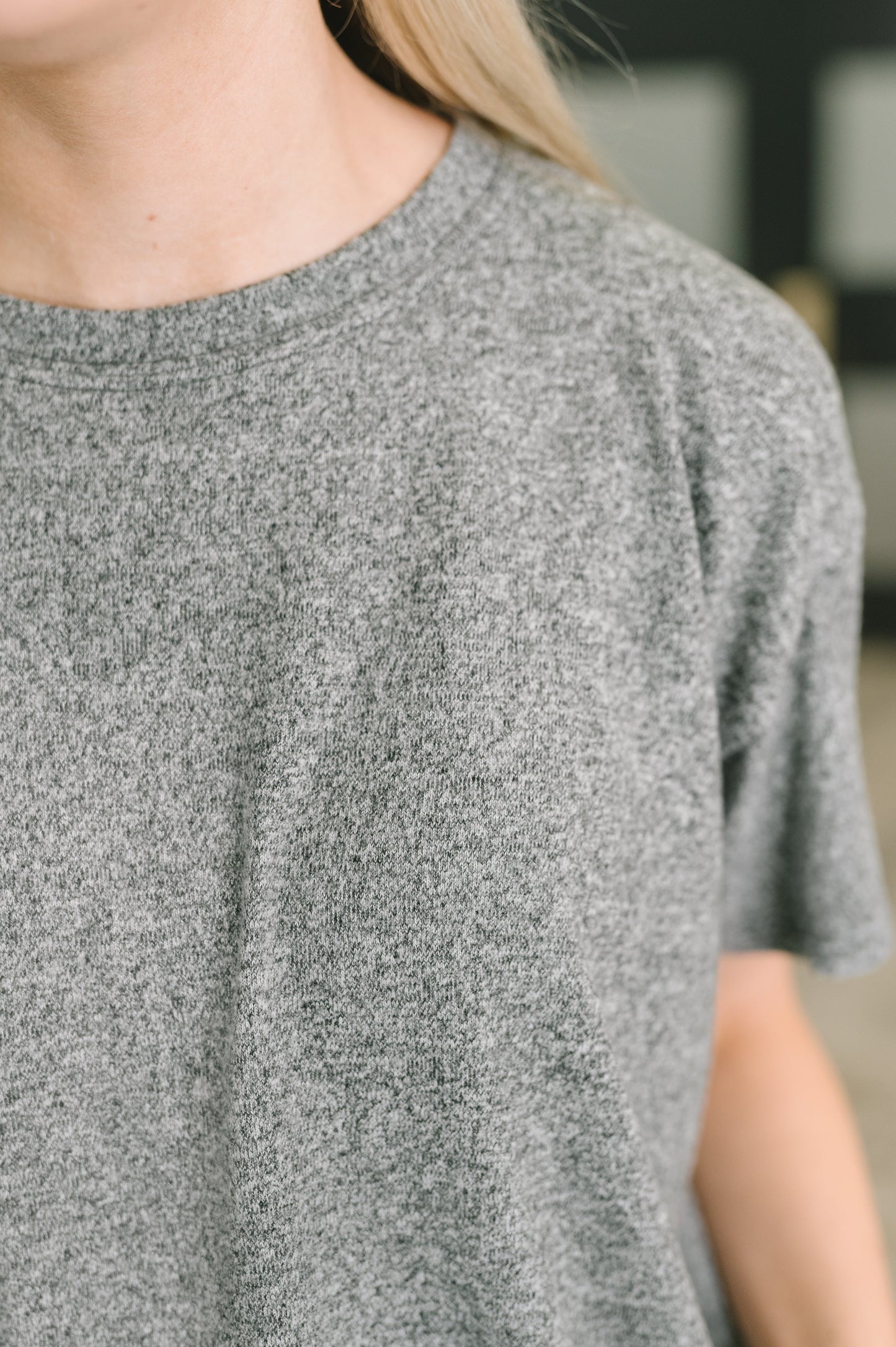 Close-up of a person wearing a short-sleeve crew-neck t-shirt in a heather gray knit fabric.