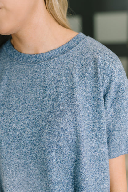 Close-up of a person wearing a heathered blue short-sleeve crewneck knit top, showing the collar and shoulder area.