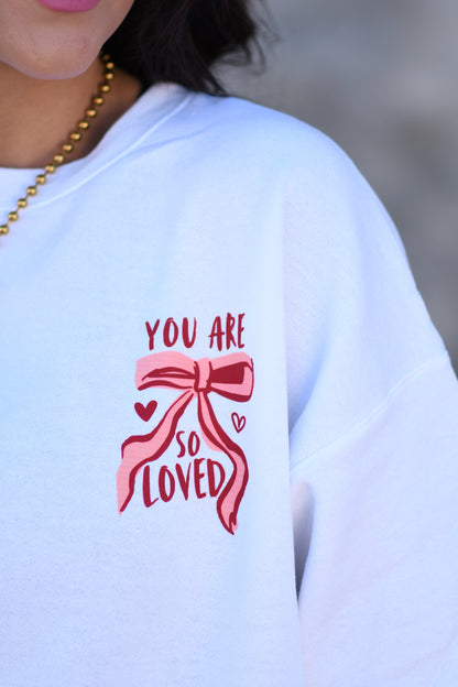 White sweatshirt with pink bow and text design on a blurred background