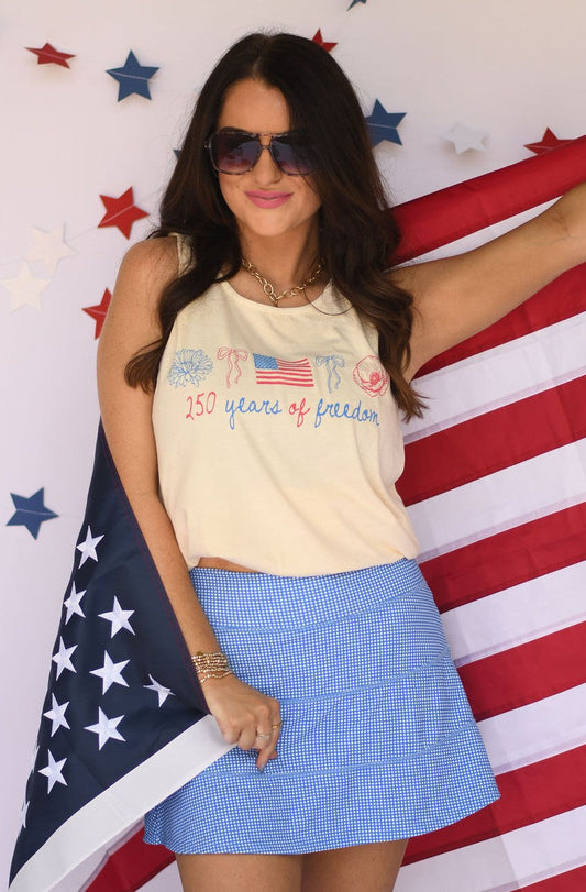 Woman wearing a tank top with text and an American flag, standing in front of an American flag background.