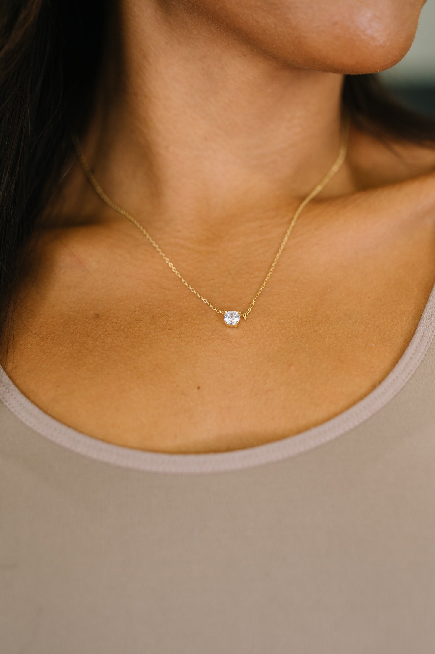 Gold necklace with a small gemstone on a person wearing a beige top.