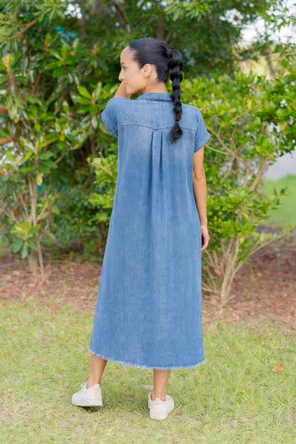 Woman wearing a blue dress standing in a grassy area with greenery.