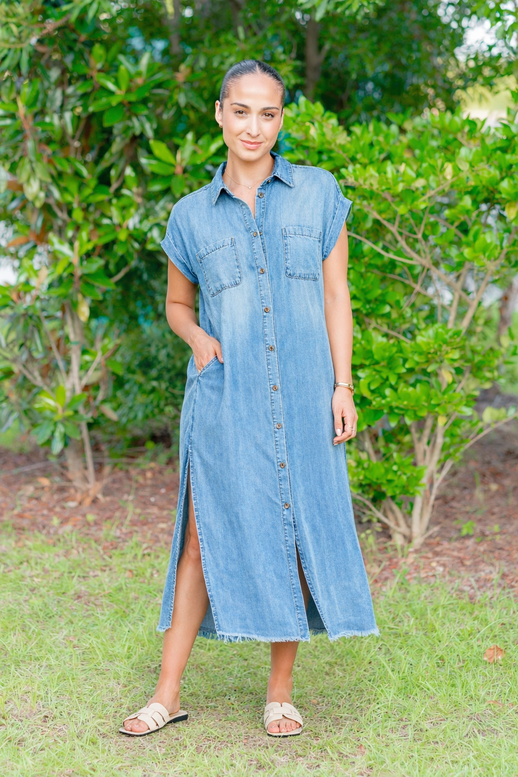 Woman wearing a denim dress standing outdoors with greenery in the background