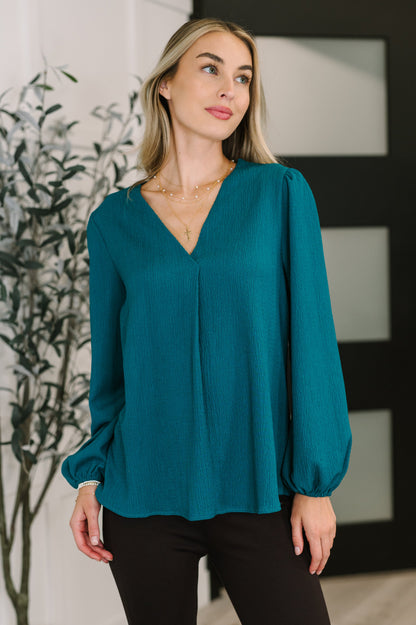 Woman wearing a teal blouse with long sleeves in an indoor setting