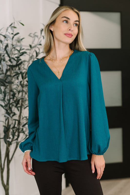 Woman wearing a teal blouse with long sleeves in an indoor setting