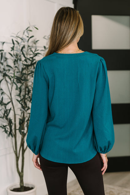 Person wearing a teal blouse with long sleeves in an indoor setting