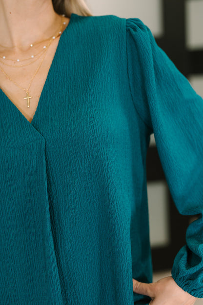 Teal blouse with long sleeves and a V-neckline, worn by a person.