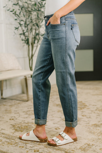 Person wearing blue jeans and white sandals standing on a stone surface.