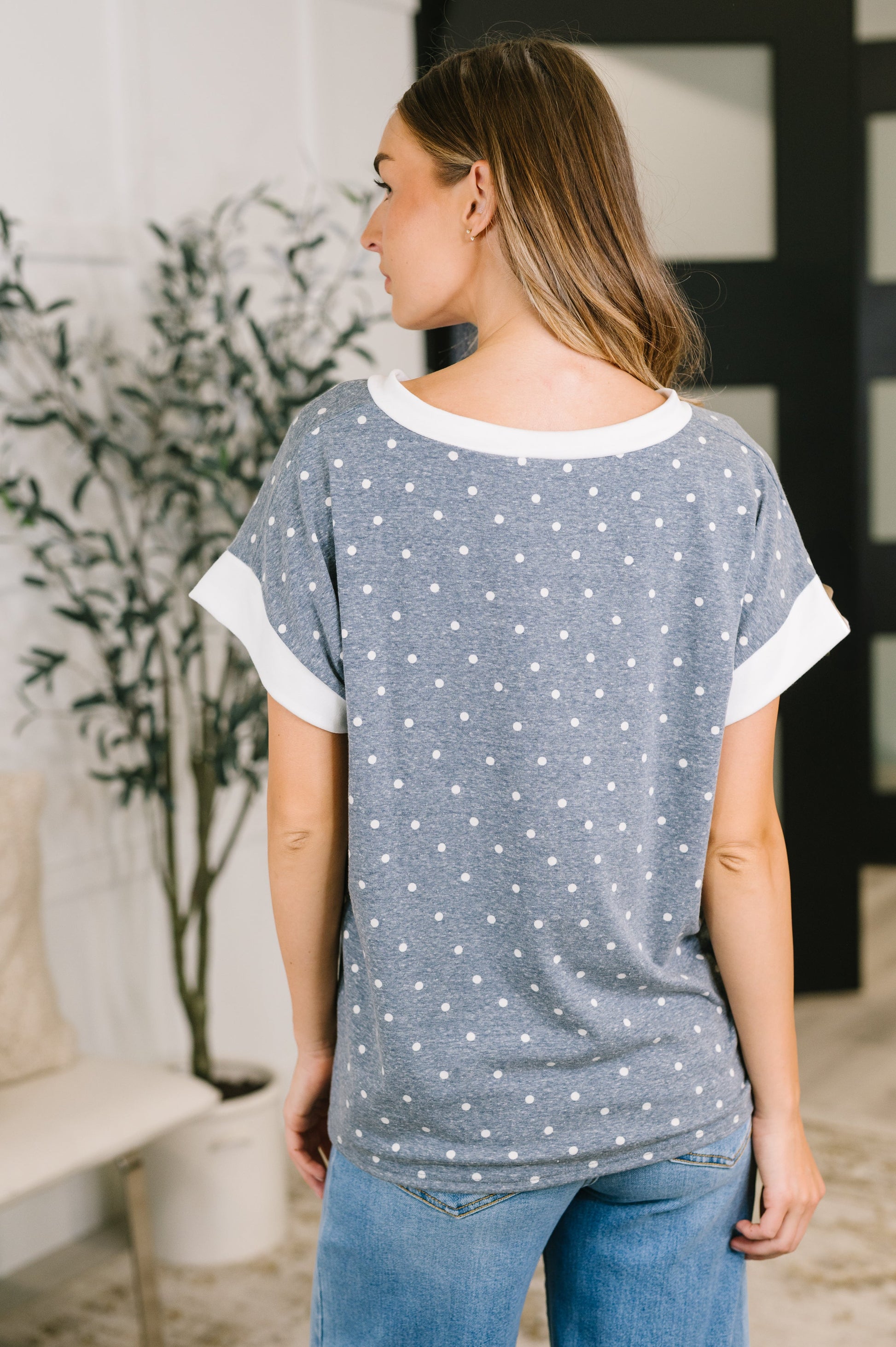 A woman wearing a heather gray short-sleeve t-shirt with white trim and a white polka dot pattern, shown from the back in an indoor setting.