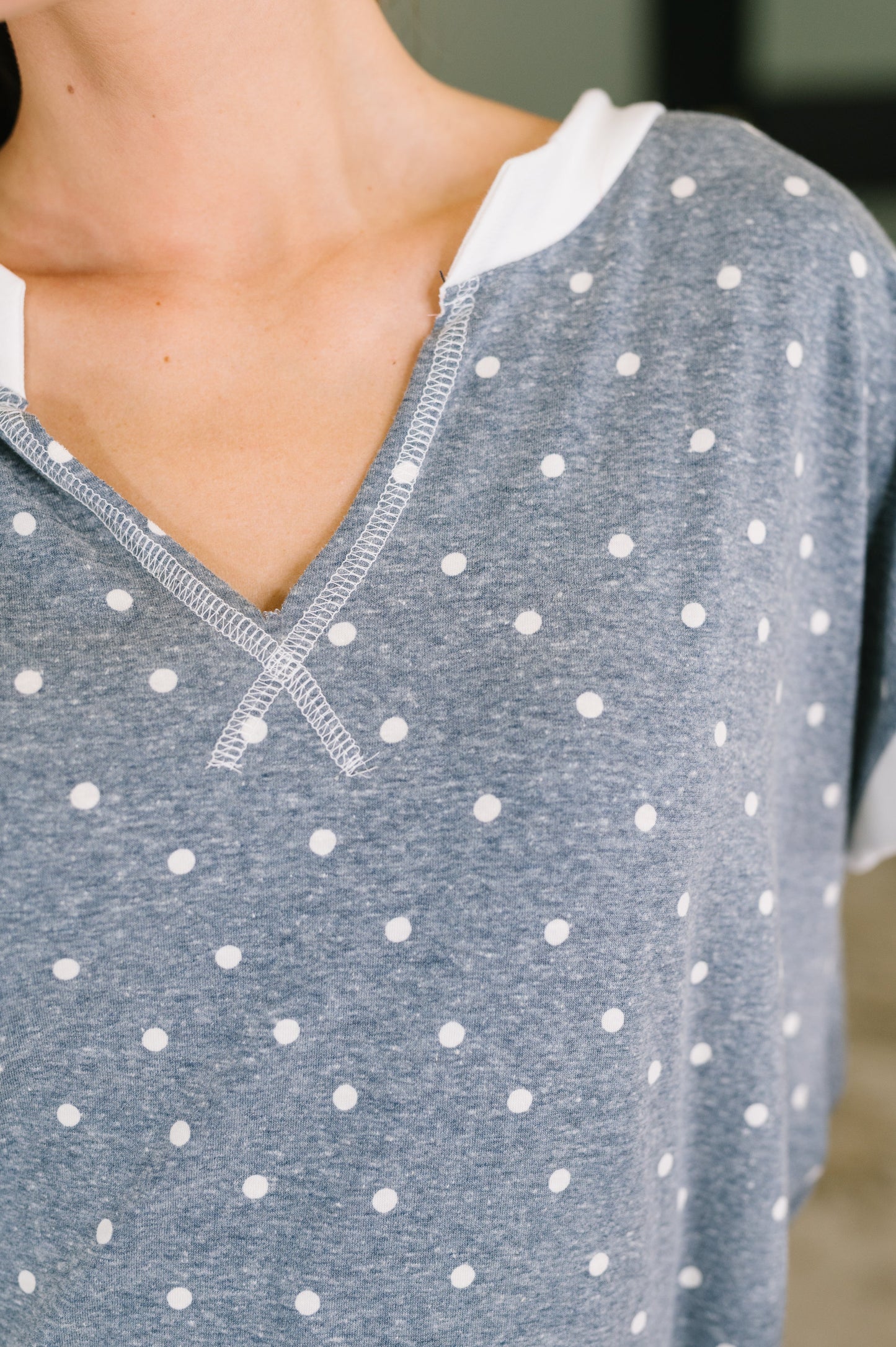 Close-up of a person wearing a heather blue short-sleeve V-neck top with white polka dots and a white inner collar.