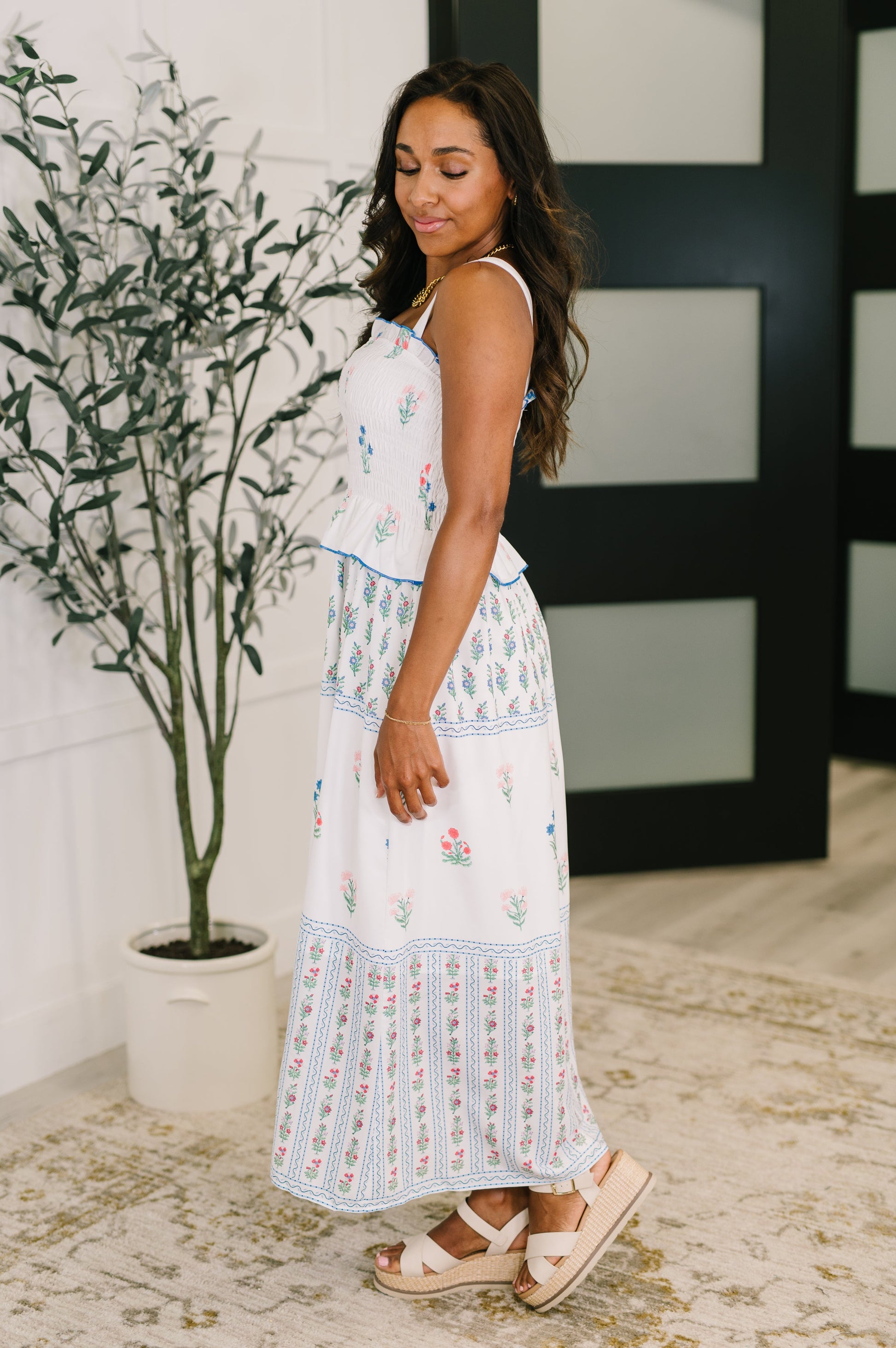 Woman in a white floral dress standing next to a plant indoors