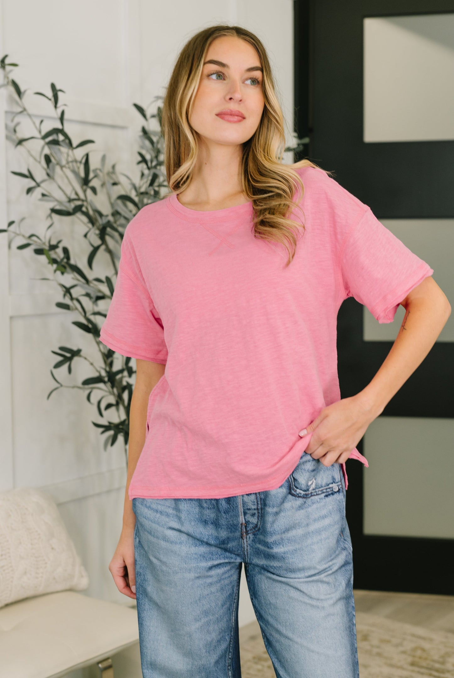 Woman wearing a pink oversized shirt and blue jeans indoors.