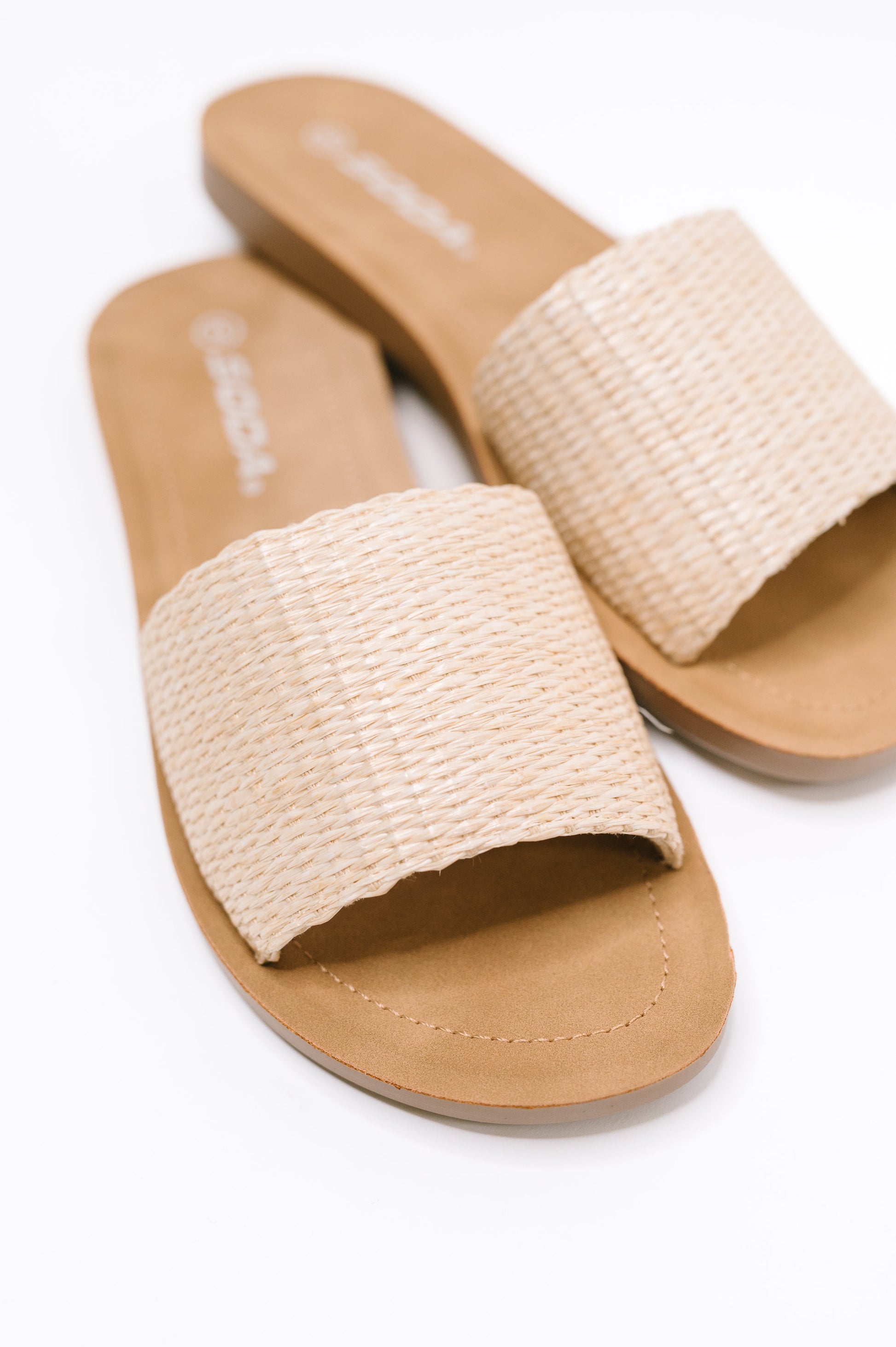 A pair of women's slide sandals with wide woven beige straps and tan footbeds, shown on a clean white background.