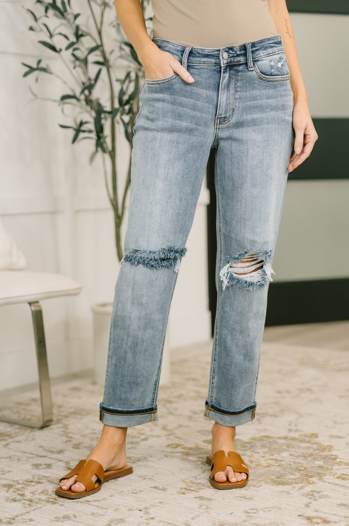 Person wearing distressed blue jeans with a blurred indoor background