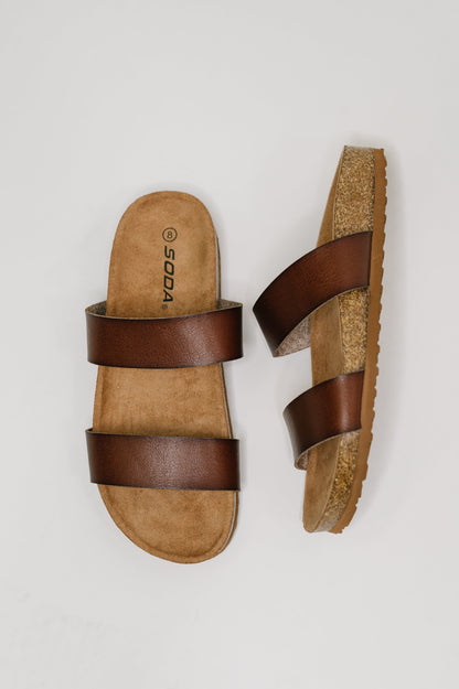 Pair of brown sandals with cork sole on a light gray background