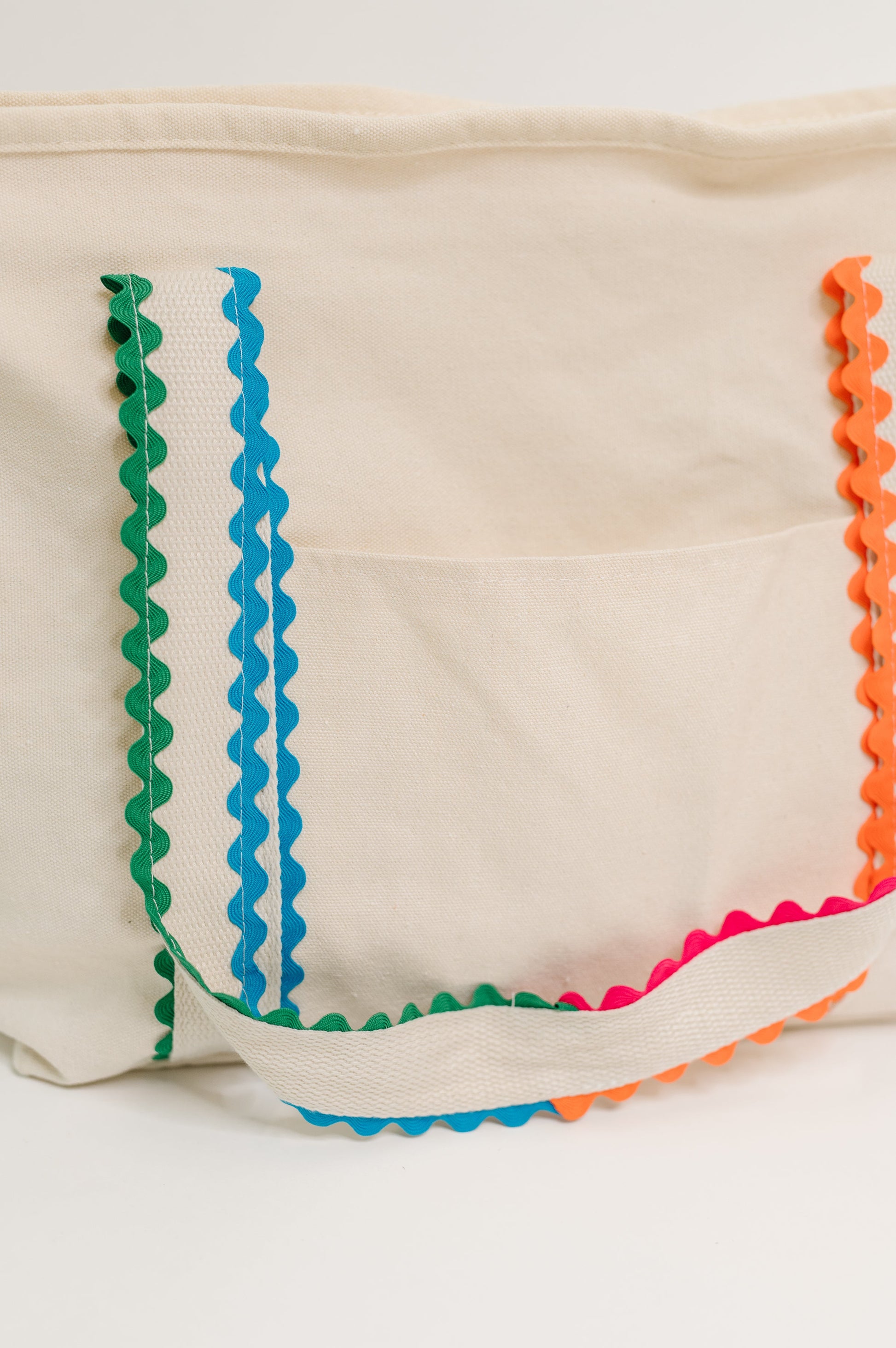 Beige tote bag with colorful zigzag trim on a white background