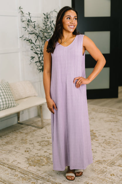 Woman wearing a purple dress standing in a room with a plant and sofa.