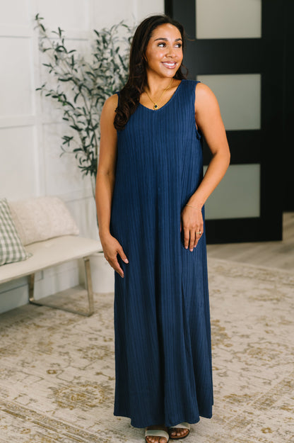 Woman wearing a blue dress standing in a room with a plant and bench.