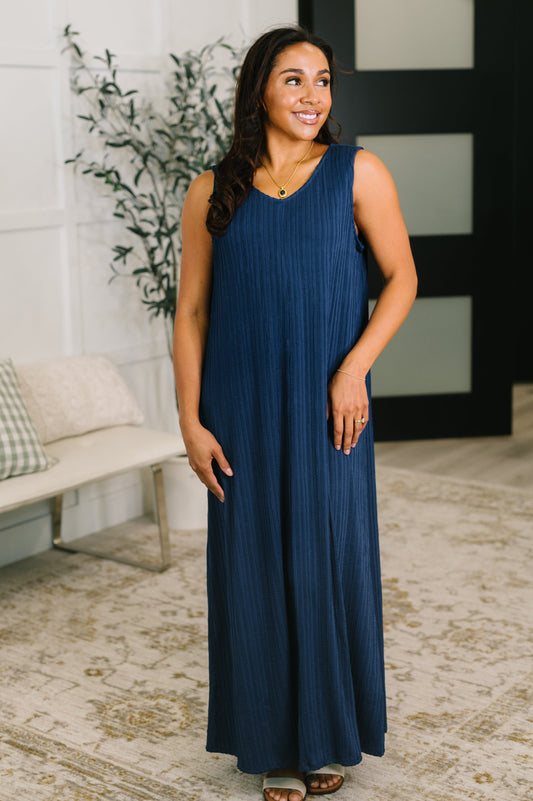 Woman wearing a blue dress standing in a room with a plant and bench.