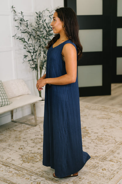 Woman wearing a long navy dress standing in a room with a plant and sofa.