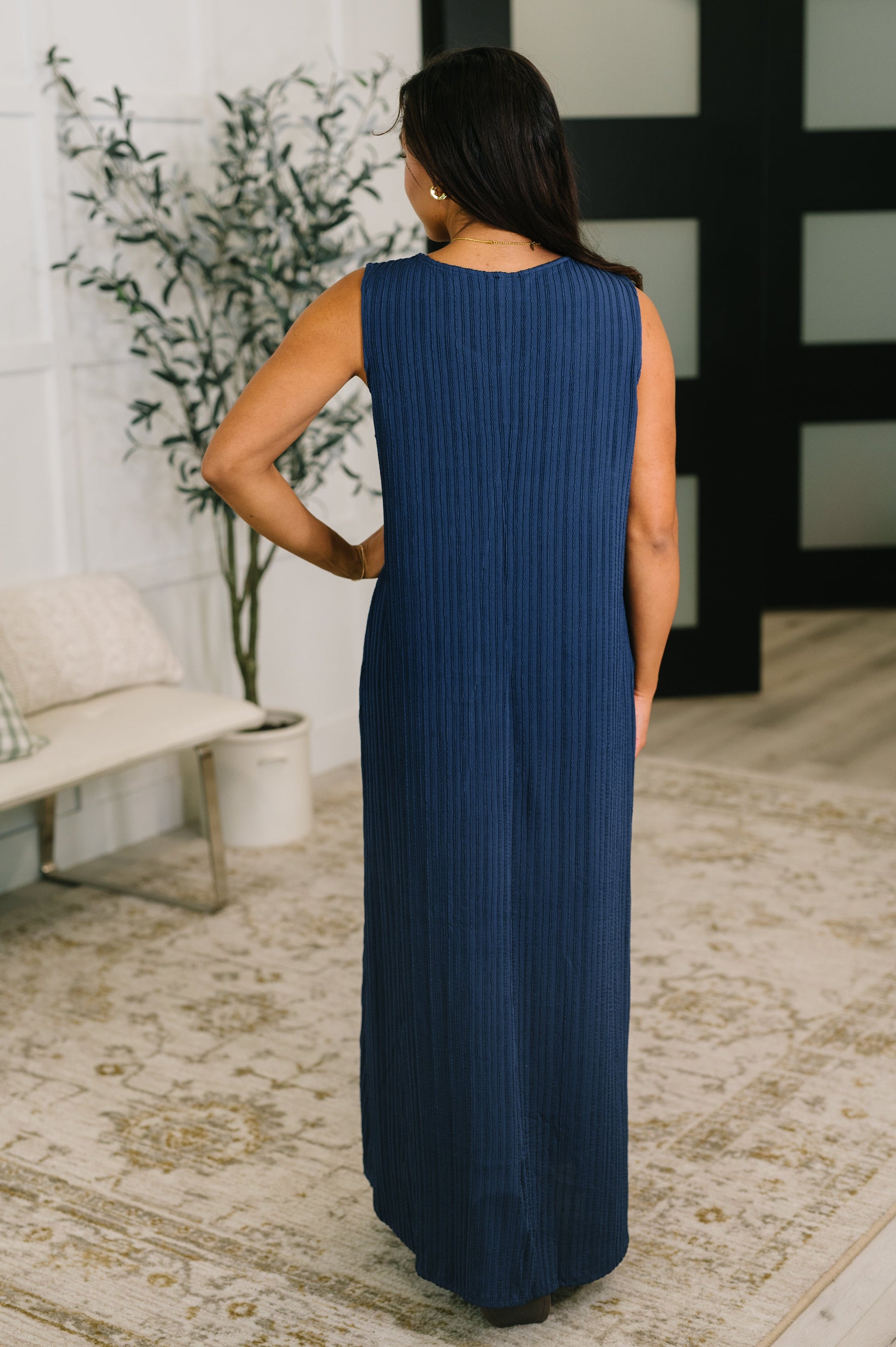 Woman wearing a blue dress standing in a room with a plant and sofa.