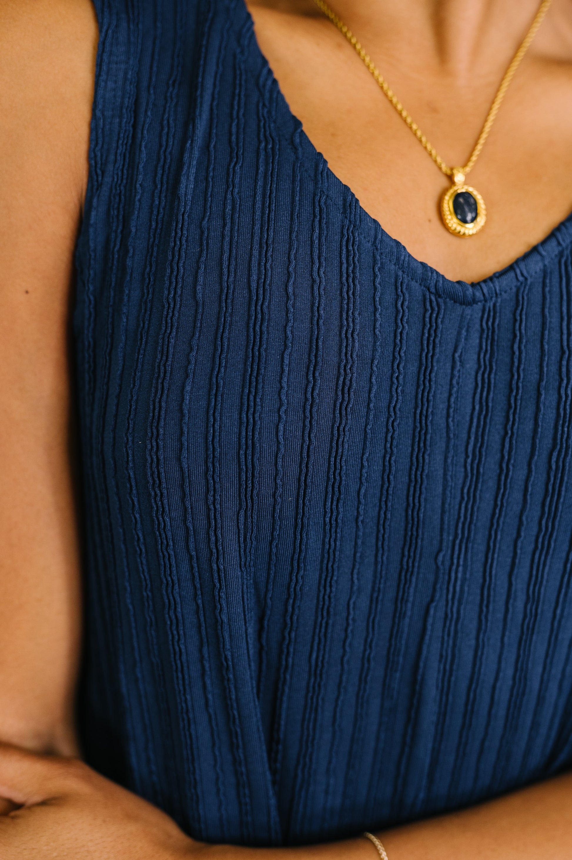 Navy blue ribbed tank top worn by a person, with a gold necklace featuring a dark pendant.