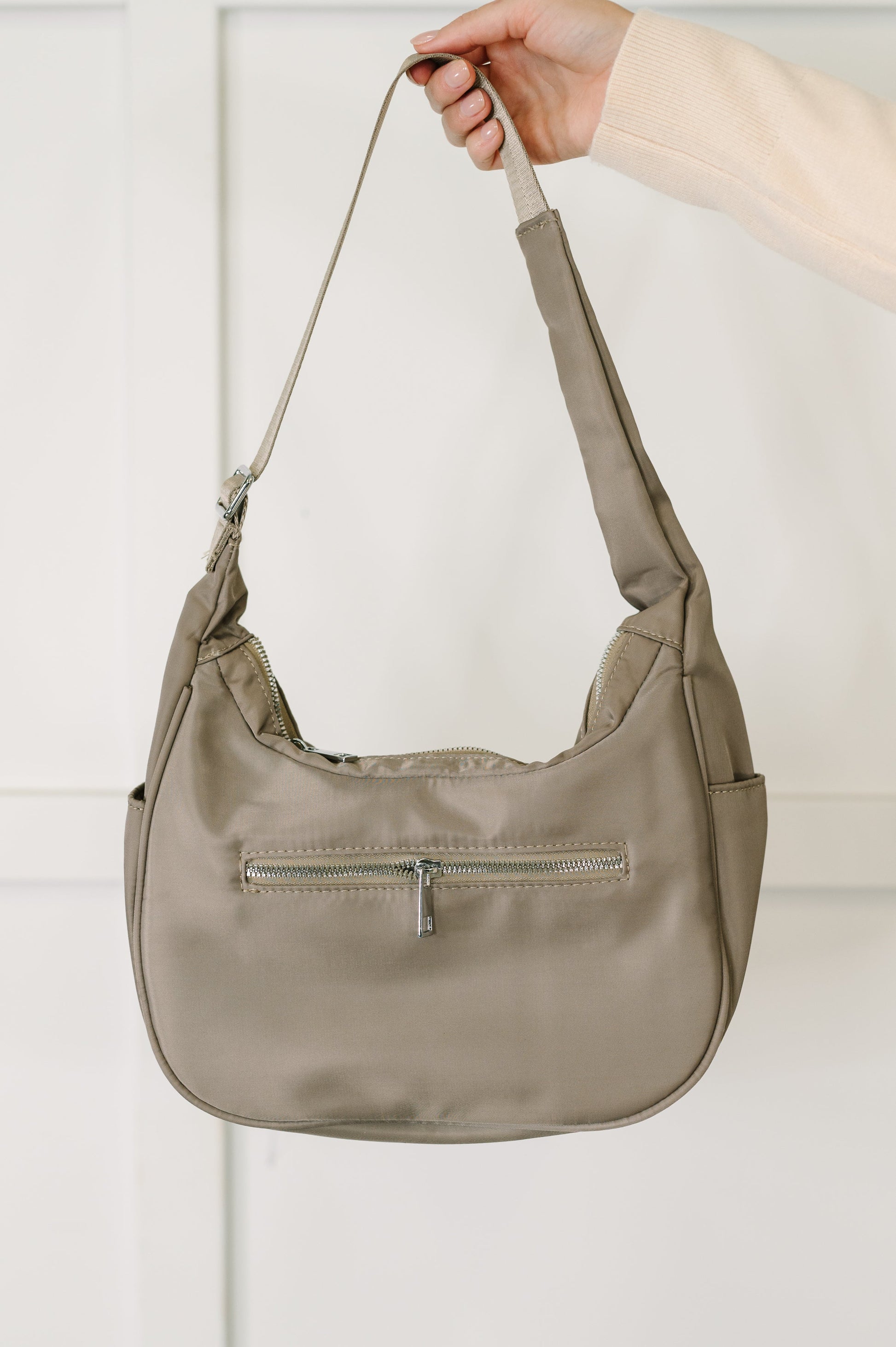 Beige handbag held by a hand against a light background