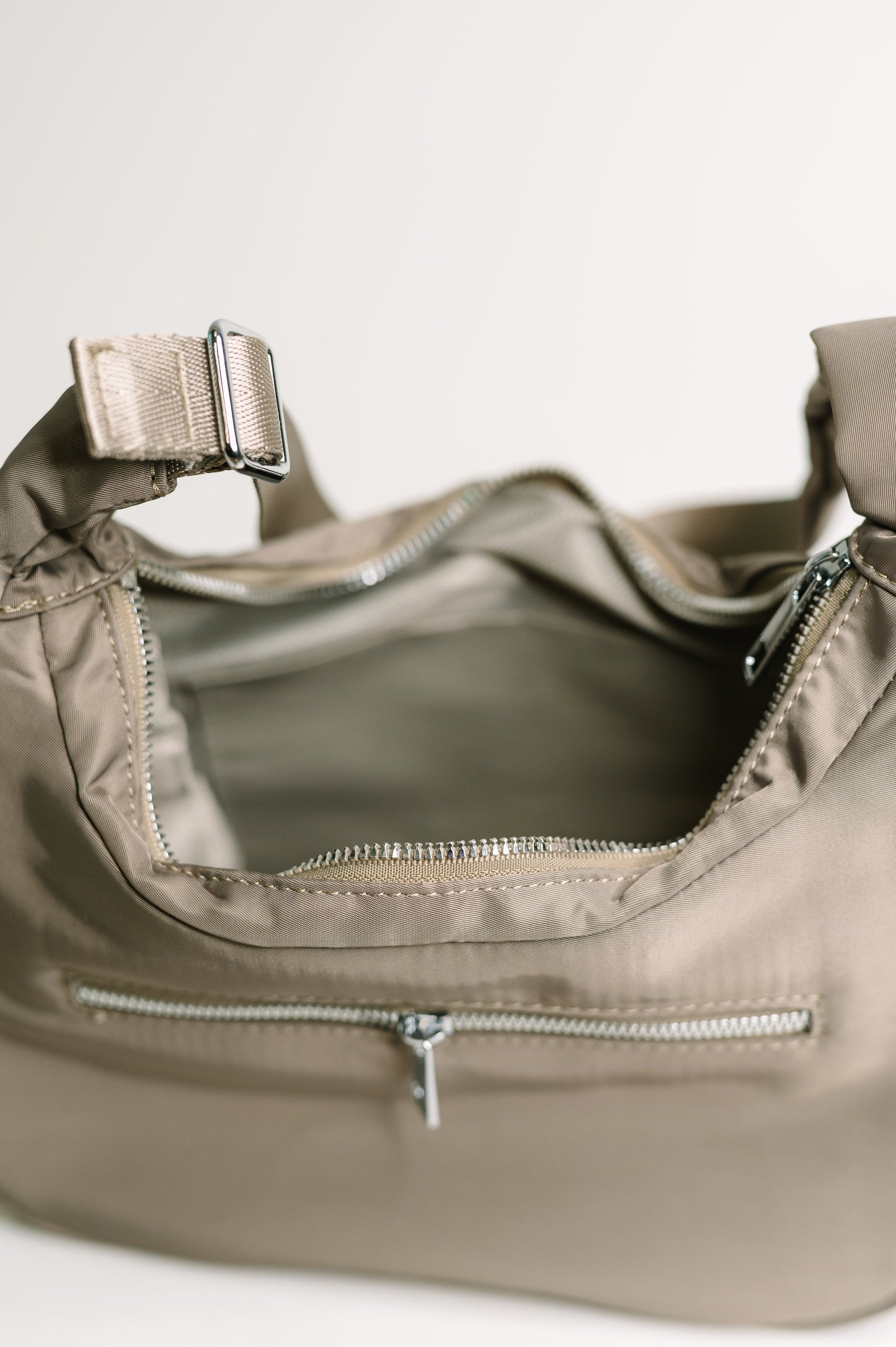 Close-up of a beige handbag with zippers on a light background